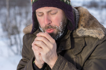 Portrait of man shivering in cold winter and breathing and rubbing hands.
