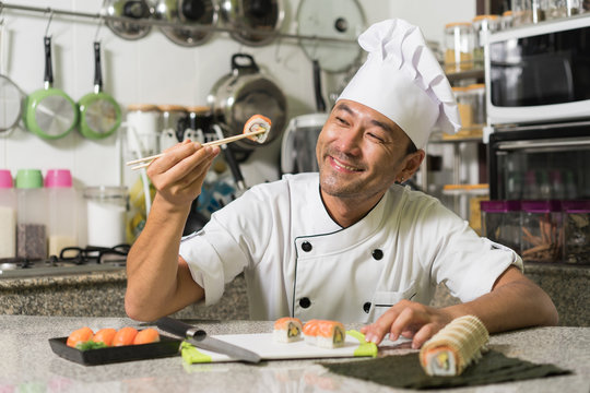 Smiling asian chef with sushi and rolls on kitchen. Focus on the face.