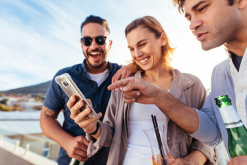 Group of friends having fun with smartphone at party