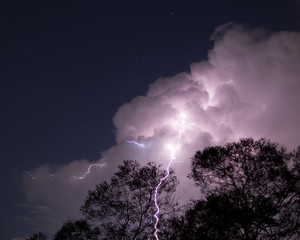 Lightning strike at night with clouds and stars in view over trees