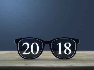 2018 white text with black eye glasses on wooden table over light blue gradient background, Happy new year business concept