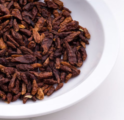 Dried small red peppers in close-up on a white plate and white table.