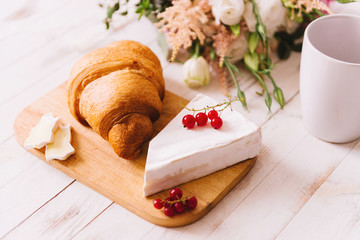 Delicious healthy wholesome breakfast with fresh flaky croissant served on a cutting board with butter, fresh berries and cheese, cup of coffee on white vintage kitchen table.
