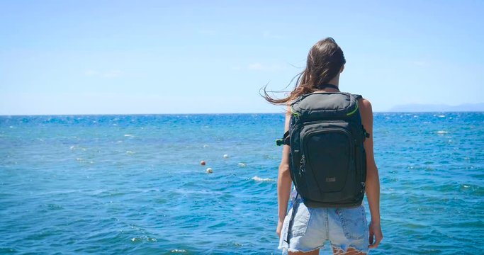 A tourist photographer woman holds a phone, feels free with a backpack on her back, a wonderfully beautiful view of the blue sea and sky. Concept: travel, vacations, freedom, telephone communication.