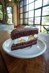 Chocolate Fudge with white cream and banana on white plate on wooden table. Eat chocolate cake in a relaxing time at the coffee shop