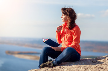 the girl sits on top of the mountain and makes notes in her notebook