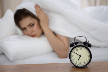 Beautiful sleeping woman lying in bed and trying to wake up with alarm clock. Girl having trouble with getting up early in the morning, Nightmare