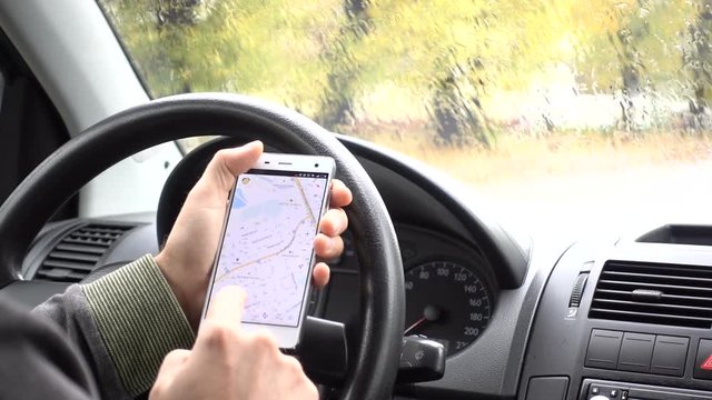 Smartphone with map gps navigation for direction, location. Man driver in modern car looking for directions in the map. Man is driving car in rainy, cloudy day. Rain. Business