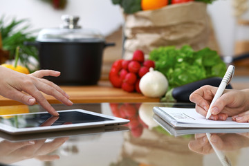 Close-up of  human hands are gesticulate over a tablet in the kitchen. Friends having fun while...