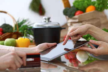 Close-up of human hands pointing into tablet  in the kitchen. Friends having fun while choosing menu or making online shopping.  Cooking, healthy meal and friendship concept