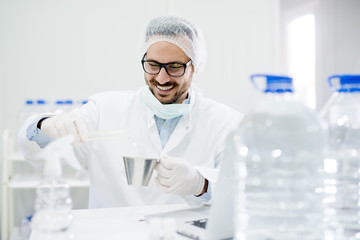 Young smiling scientist with glasses working with tubes and water in the laboratory.