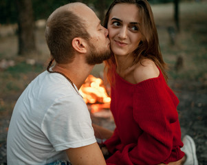 Obraz premium Enamored couple sits and kisses on picnic in forest on bonfire flame background.