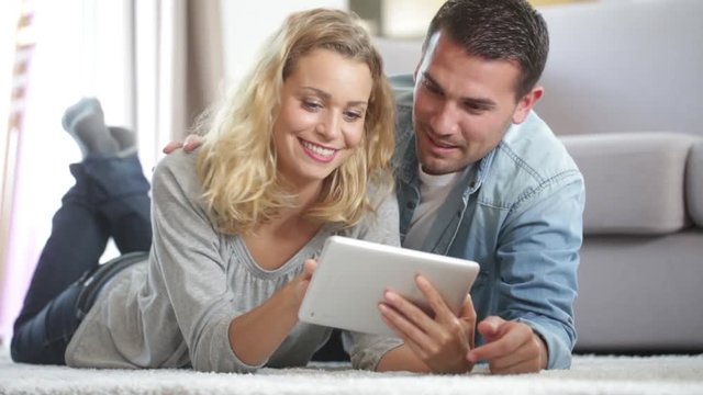 Happy young couple layed on the carpet of their living room and using a tablet