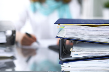 Binders with papers are waiting to be processed with businesswoman or secretary back in blur....