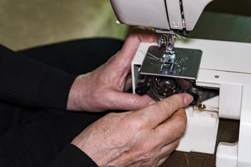 Woman's hands open the socket to replace the spool of thread in the sewing machine.
