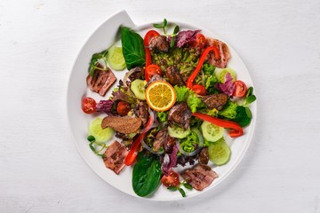 Salad with bacon and chicken liver. On a wooden surface. Top view. Free space for your text.