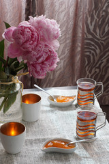 A cup of hot tea next to a saucer with dessert and a bouquet of peonies, breakfast for two
