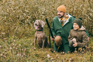 Father and son squatting in bushes at hunt