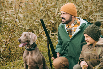 Father and son squatting in bushes at hunt