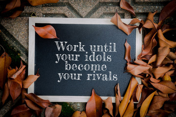 Inspirational motivation quote WORK UNTIL YOUR IDOLS BECOME YOUR RIVALS, Chalks board and dry leaves on the ground
