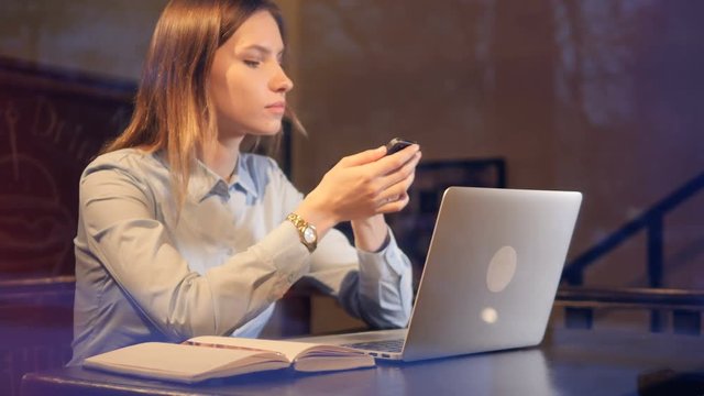 Young lady using laptop and smartphone late in the evening. 4K.