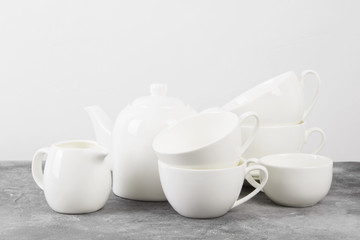 Clean white tableware (teapot, cups, saucers) on a gray background