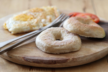 Breakfast; donut, fried egg and tomato with knife and fork on wooden plate.