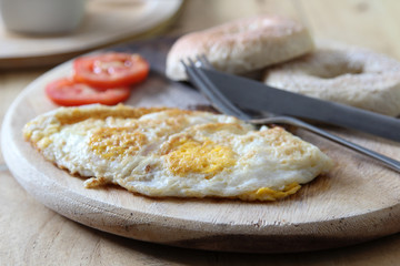 Breakfast; donut, fried egg and tomato with knife and fork on wooden plate.