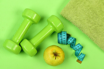 Barbells, apple and tape measure near green towel
