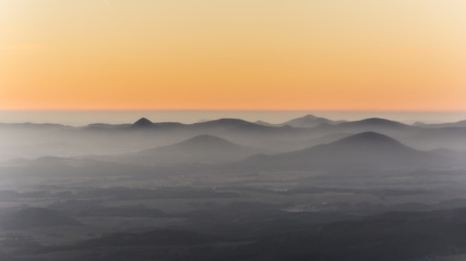 Hills covered with fog. Foggy landscape under orange sunset sky.