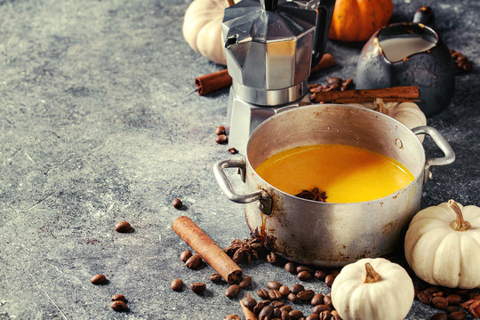 Ingredients for cook spicy pumpkin latte. Coffeepot, pumpkin milk in pan, jug of cream with spices, coffee beans and decorative pumpkins above over gray texture background. Close up