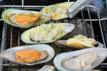 Street food, grilled mussels with cheese on stove at market.