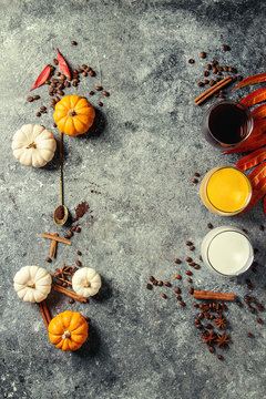 Ingredients for cook spicy pumpkin latte. Glasses with black coffee, pumpkin milk, cream with spices, coffee beans, autumn leaves above over gray texture background. Top view, space.