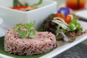 Thai cuisine, red steamed rice on banana leaf with coriander on topped.