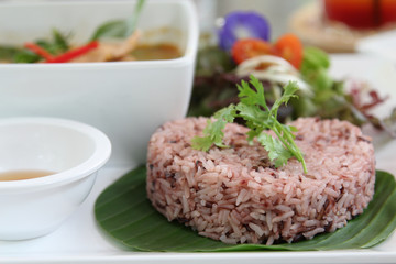 Thai cuisine, red steamed rice on banana leaf with coriander on topped.
