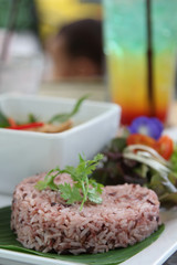 Thai cuisine, red steamed rice on banana leaf with coriander on topped.