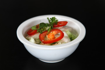 Thai cuisine, vinegar with cucumber, onion, chili and coriander in white bowl on black background.