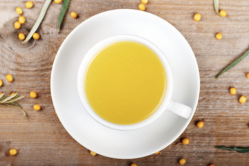 sea-buckthorn tea in a white cup on the table. near lay berries of sea-buckthorn