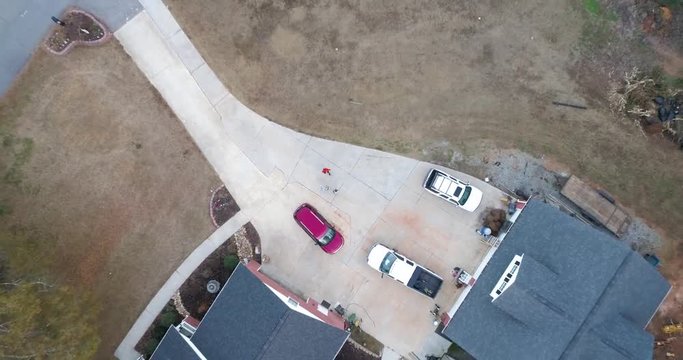 Drone footage flying up above cars and a house