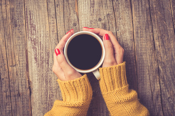 Female hands in warm sweater holding cup of coffee. Close up