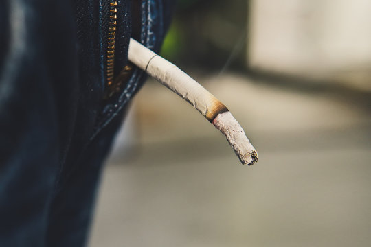 Guy holds a Smoking cigarette butt from the cigarette with two fingers.