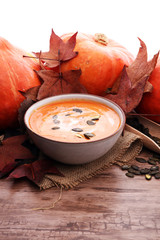 Roasted pumpkin and carrot soup with cream and pumpkin seeds on wooden background