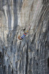 Fototapeta premium Bungee jumping in Prohodna Cave, Bulgaria. Young woman with long blond hair hanging on a cord, the dark rocks of the cave seen at background