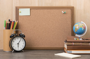 blank cork board with alarm clock, book on wooden desk.