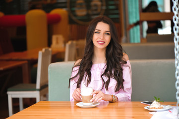 Woman drinking hot cappuccino coffee and eating cake at cafe.