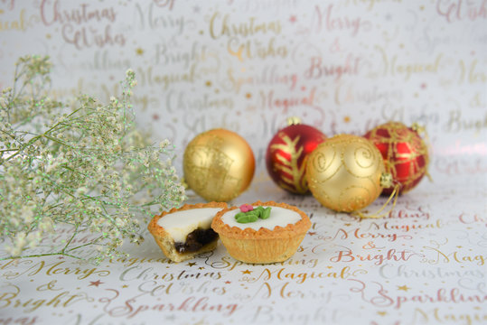 Christmas Food Photography Image With Traditional Iced Mince Pie With Festive Text In Background And With Flowers And Red Gold Tree Decorations Of Baubles