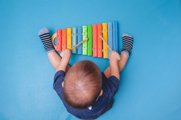 Bird eye view of Cute little Asian 18 months / 1 year old baby boy child hold sticks & plays a musical instrument colorful wooden toy xylophone - Powered by Adobe