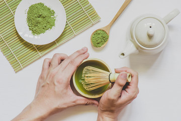 male hands holding cup of green matcha tea on white wooden background