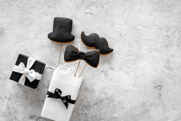 Birthday gift for men. Wrapped box, cookies in shape of black tie, mustache, hat. Grey background top view copyspace