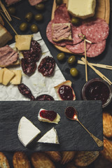 Bread crackers, ham ham, sausage, cheese, olives, veined tomato and plums on a dreess black background. View from above